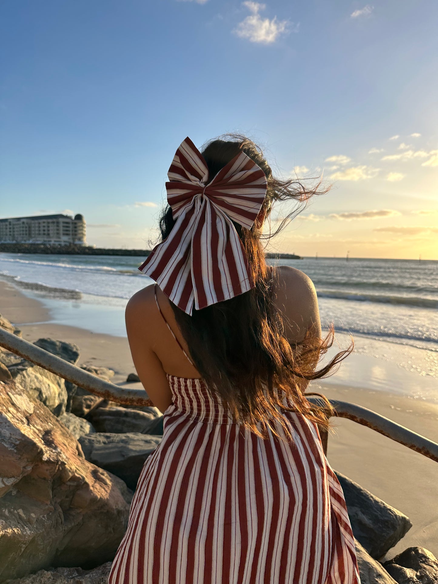 Person wearing a large striped hat and dress on a beach at sunset.