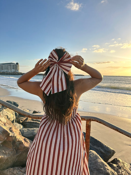 Woman in a red and white striped dress with a large bow at the beach during sunset.