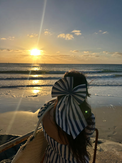 Person with a striped hat and long coat standing on a beach at sunset.