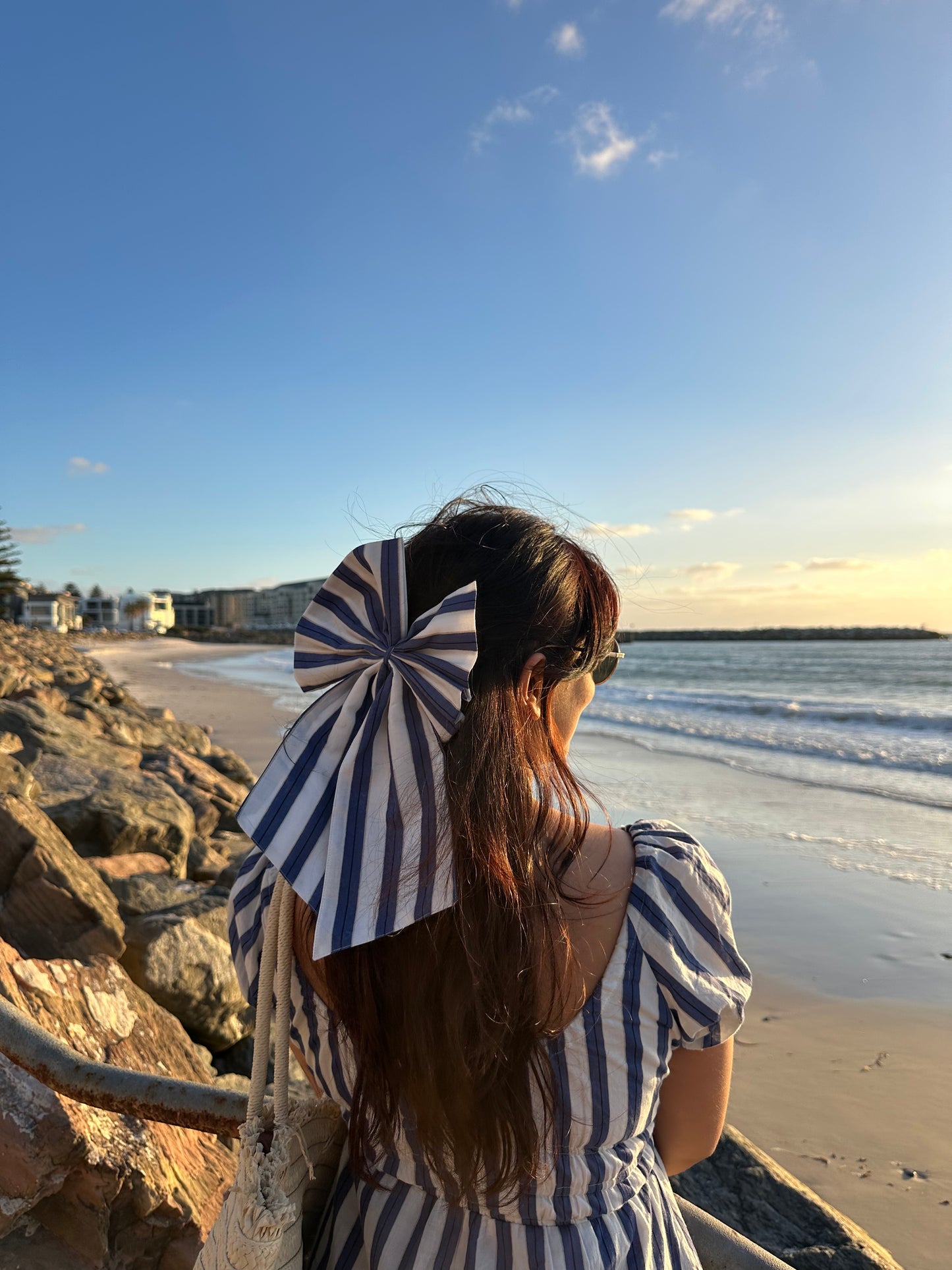 Woman with a large striped bow in her hair standing on a beach.