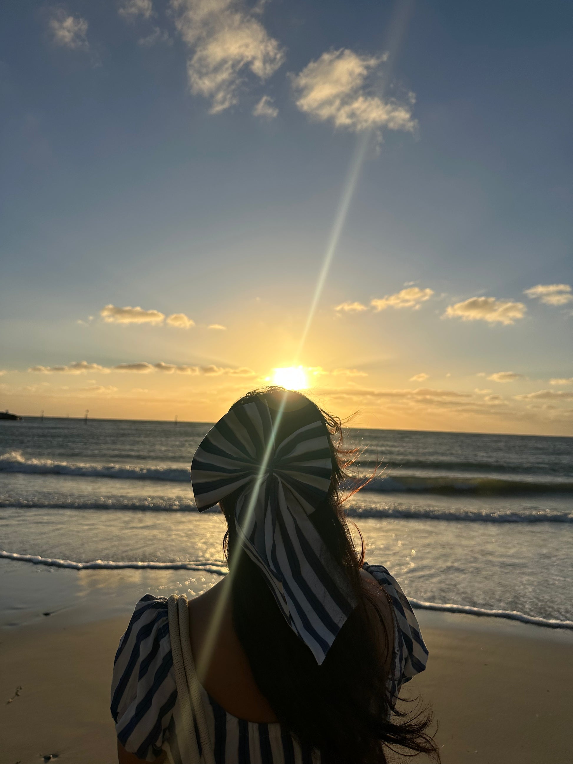 Person standing on a beach at sunset with sun lens flare