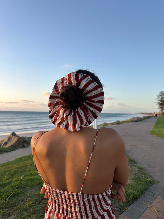 Person wearing a red and white patterned headscarf and dress by the beach.