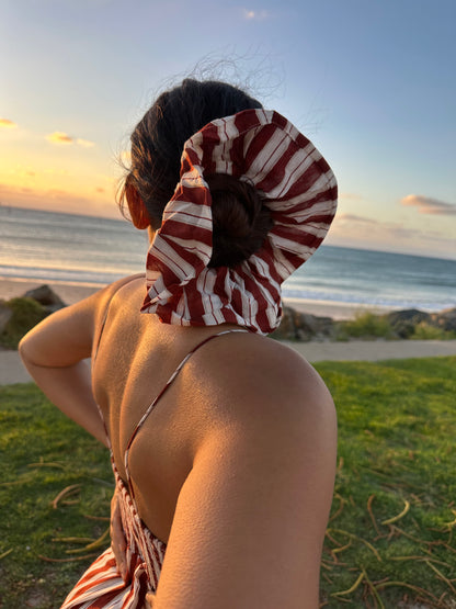 Person with a striped scrunchie on their head at a beach during sunset