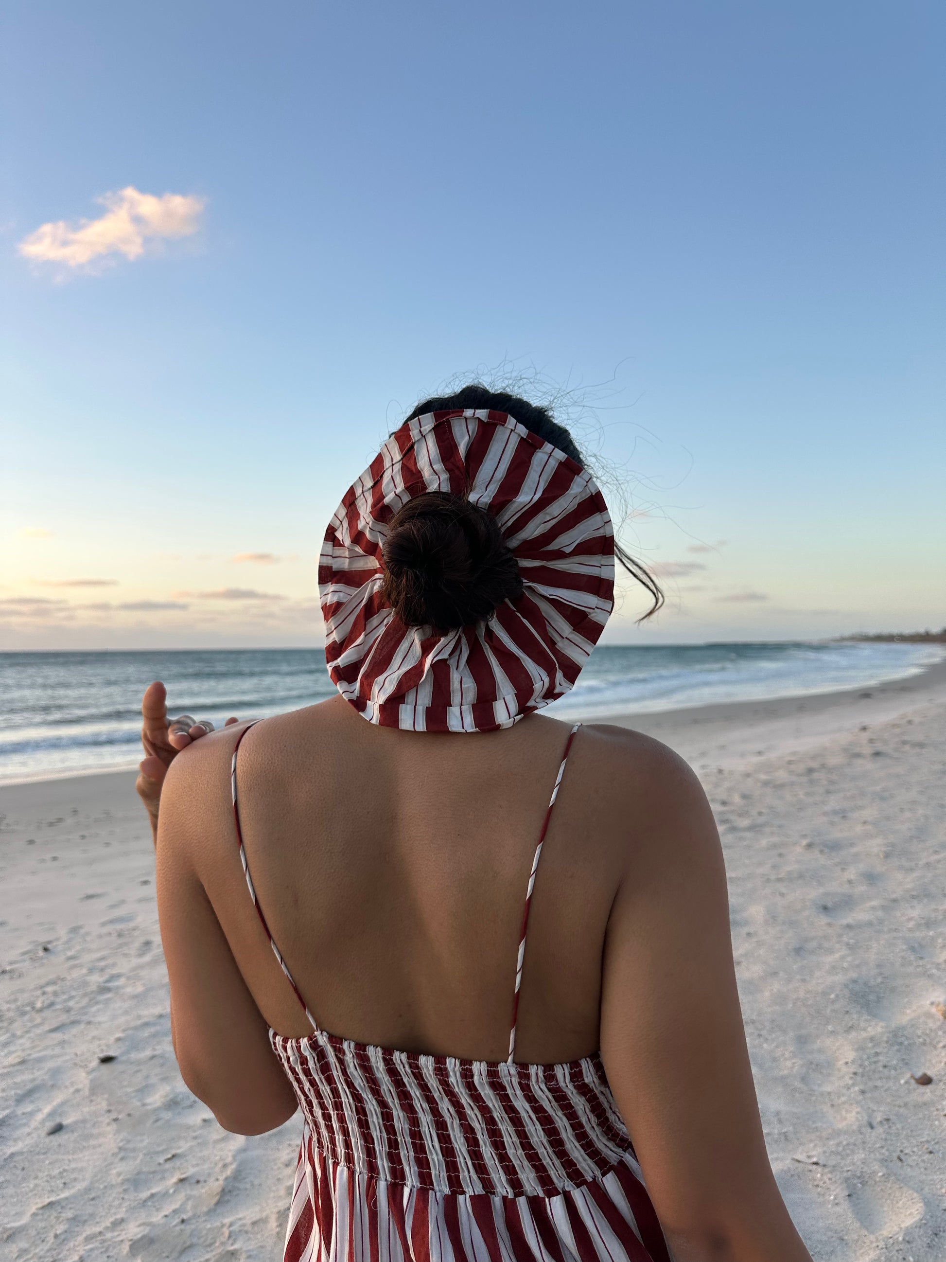 Person wearing a red and white striped dress and headscarf on a beach