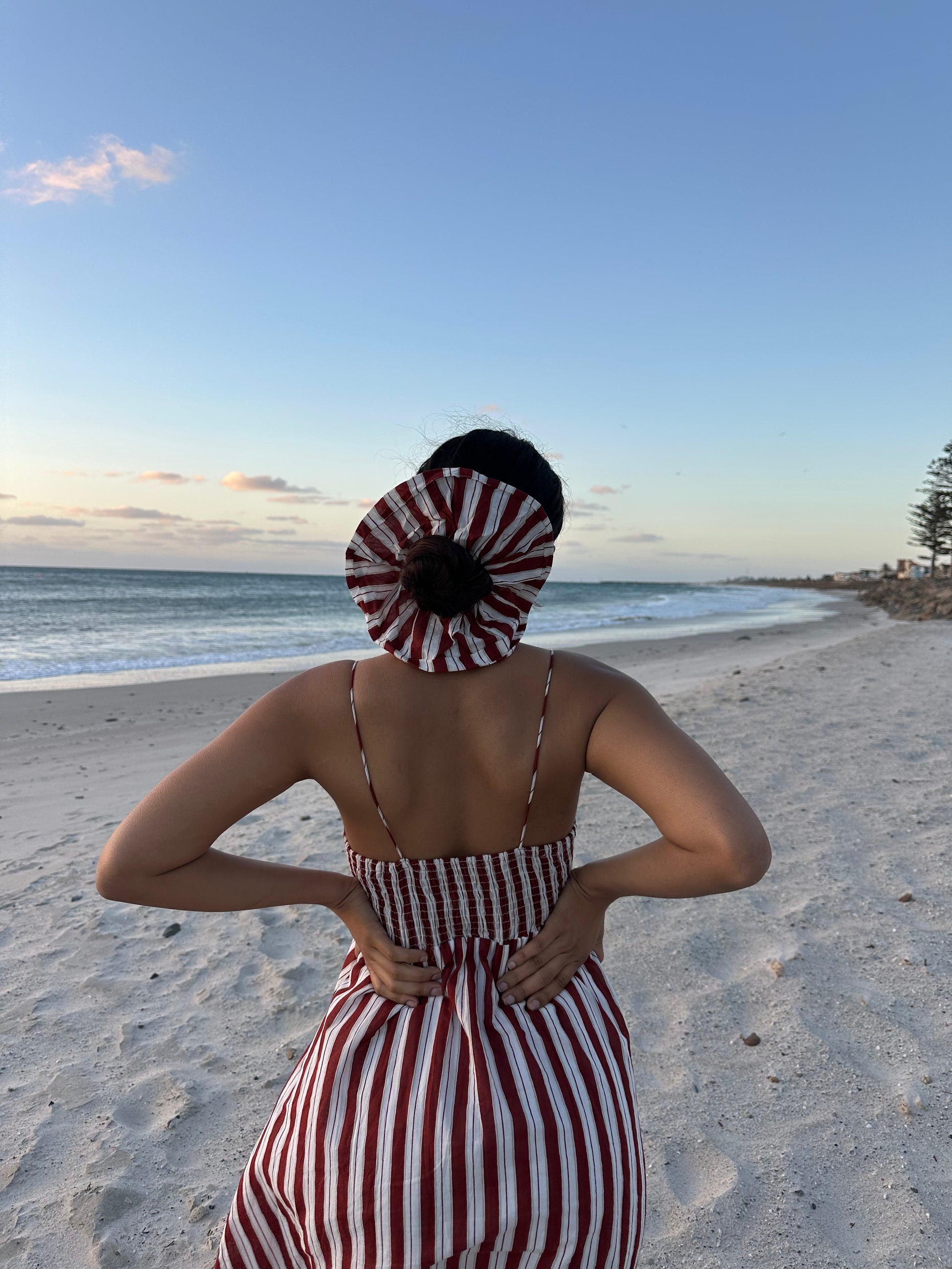 Person wearing a red and white striped dress and headscarf on a beach.
