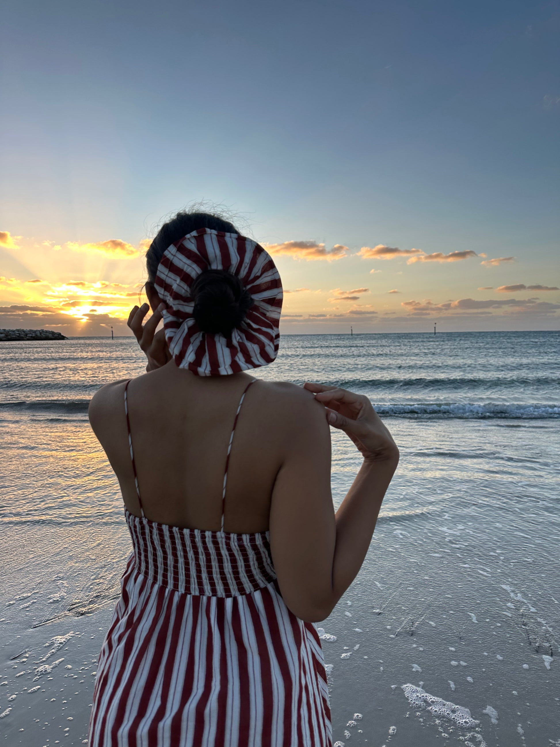 Person wearing a striped dress and hat on a beach at sunset