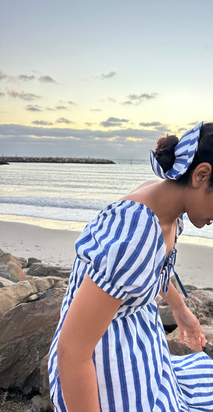 Woman in a blue and white striped dress sitting on a beach with a scenic background.