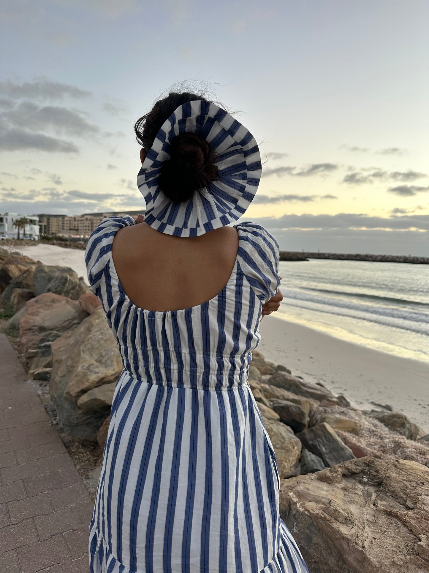 Person wearing a blue and white striped dress and sun hat at a beach.