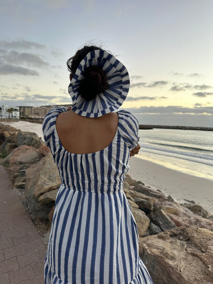 Person wearing a blue and white striped dress and sun hat at a beach.