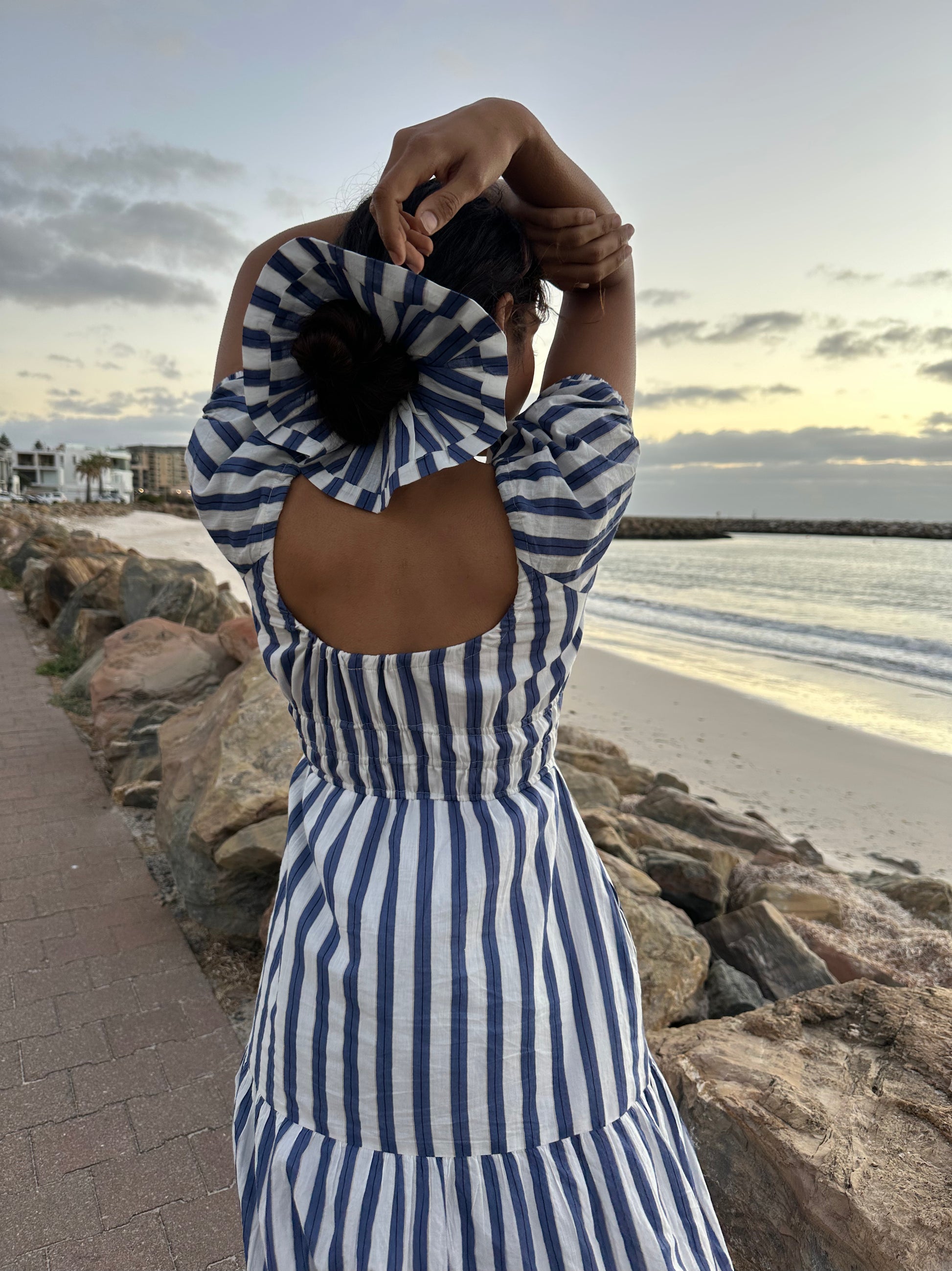 Person wearing a blue and white striped dress on a beach at sunset.